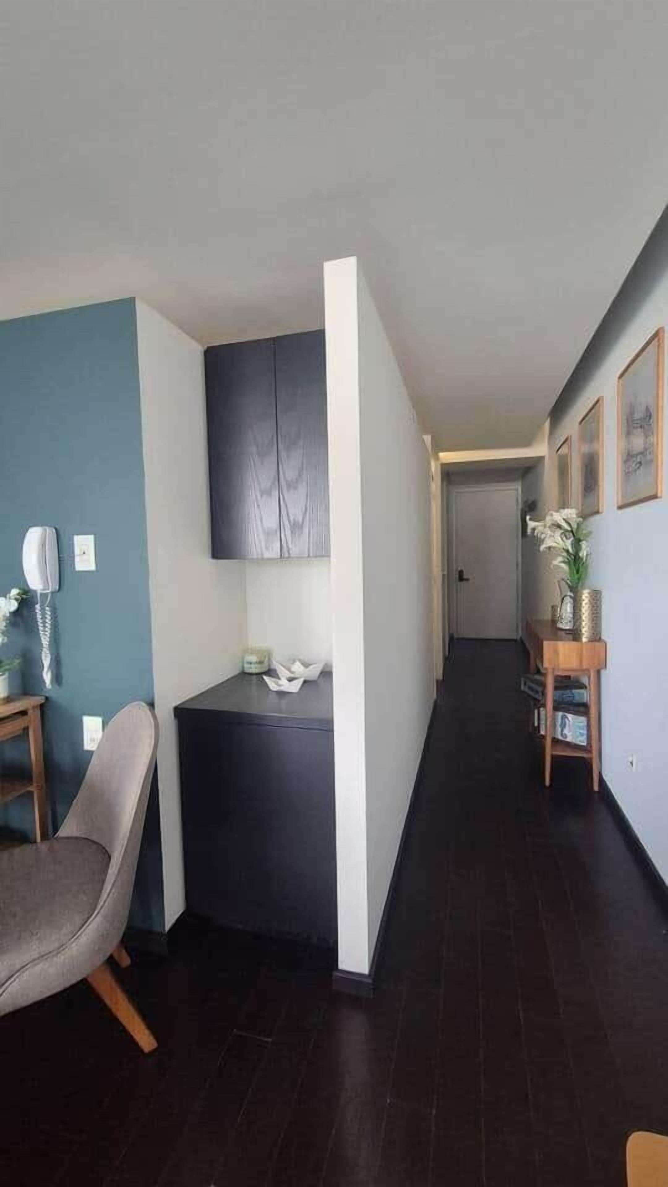 A hallway with a dark wooden floor, a grey chair, a small table with a telephone, and a cabinet.