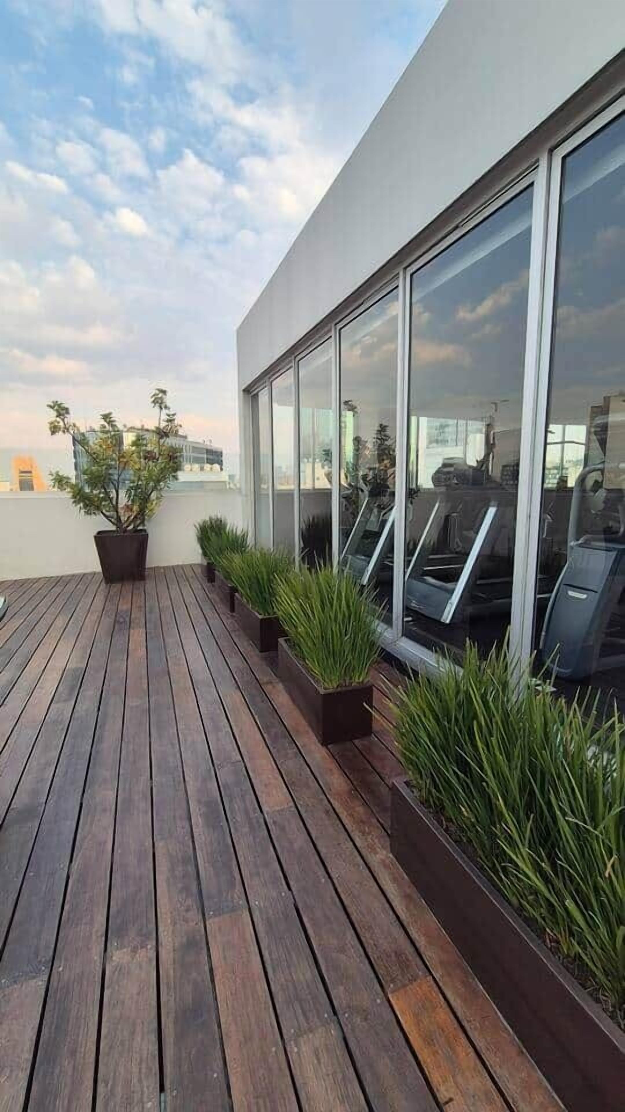 A rooftop terrace with wooden flooring, potted plants, and exercise equipment.