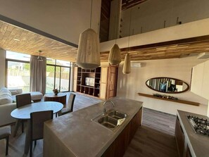 Una cocina moderna con una isla central, un comedor con mesa redonda y un gran ventanal que proporciona luz natural.