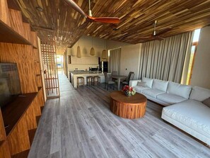 A modern interior with a wooden ceiling, a dining area, a sofa, and a kitchen in the background.