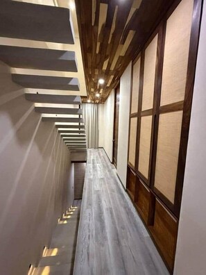 Ein schmaler Gang mit Holzbalkendecke und ein langer, schmaler Raum mit Tatami-Matten.