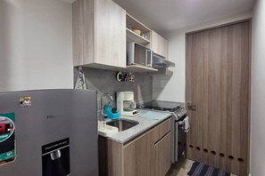 Une cuisine de taille réduite, équipée d’un réfrigérateur, d’un évier, d’une cuisinière et de meubles de rangement en bois.