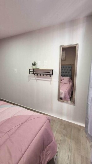 Ein Schlafzimmer mit einem Bett, einem Nachttisch, einem Spiegel und einem an der Wand befestigten Regal.