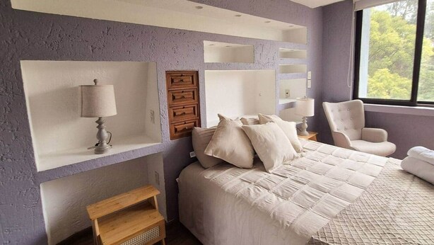 Une chambre à coucher avec un lit, une chaise, une table de chevet et une étagère avec une lampe.