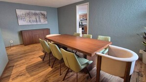 Un coin repas avec une table en bois et des chaises vertes, une cuisine en arrière-plan et un mur gris.