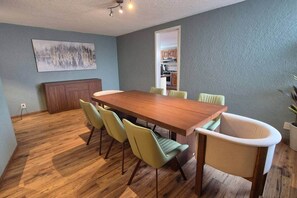 A dining area with a wooden table and green chairs, a kitchen in the background, and a grey wall. - Fabian (Rio de Janeiro) (Mexico City)