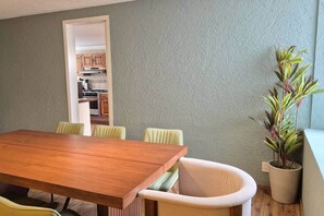 Un coin repas avec une table et des chaises en bois, une plante en pot et une vue sur la cuisine.