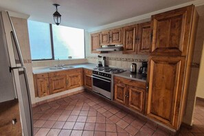 A kitchen with wooden cabinets, a stainless steel stove, and a window providing natural light. - Fabian (Rio de Janeiro) (Mexico City)