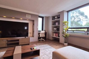 A modern living room with a large flat-screen TV, a comfortable sofa, a small coffee table, and a bookshelf. - Fabian (Rio de Janeiro) (Mexico City)