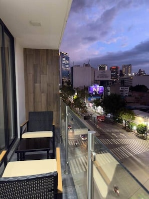 Een balkon met zitplaatsen, uitzicht op de stad, en een gebouw met verlichte reclame.