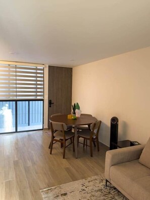 A living room with a sofa, a dining table with chairs, a sliding glass door, and a small table with a speaker. - Erick Insurgentes A 606 (Mexico City)