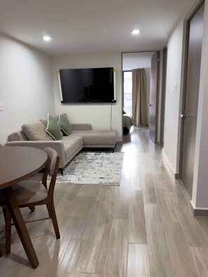 Een moderne woonkamer met een bank, een eettafel en een flatscreen televisie aan de muur.