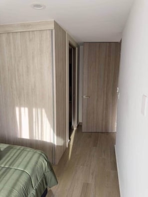 Een smalle gang met houten vloer en deuren naar een slaapkamer.