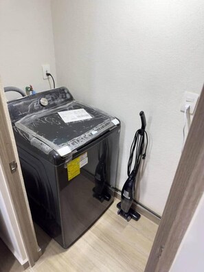 A compact washing machine in a small laundry room with a power outlet and a vacuum cleaner. - Erick Insurgentes A 606 (Mexico City)