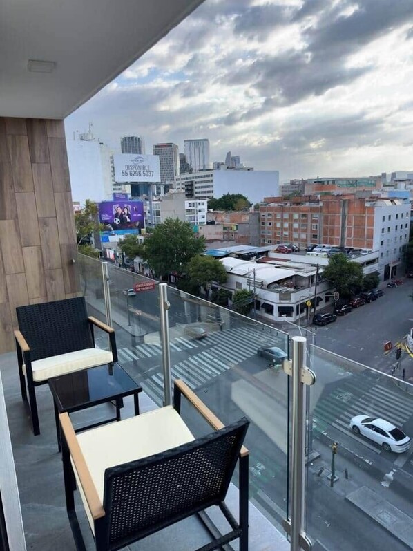 A balcony with two chairs and a table, overlooking a city street with buildings and a billboard. - Erick Insurgentes A 606 (Mexico City)