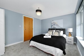 Un dormitorio con cama, mesita de noche, lámpara, ventana y puerta.