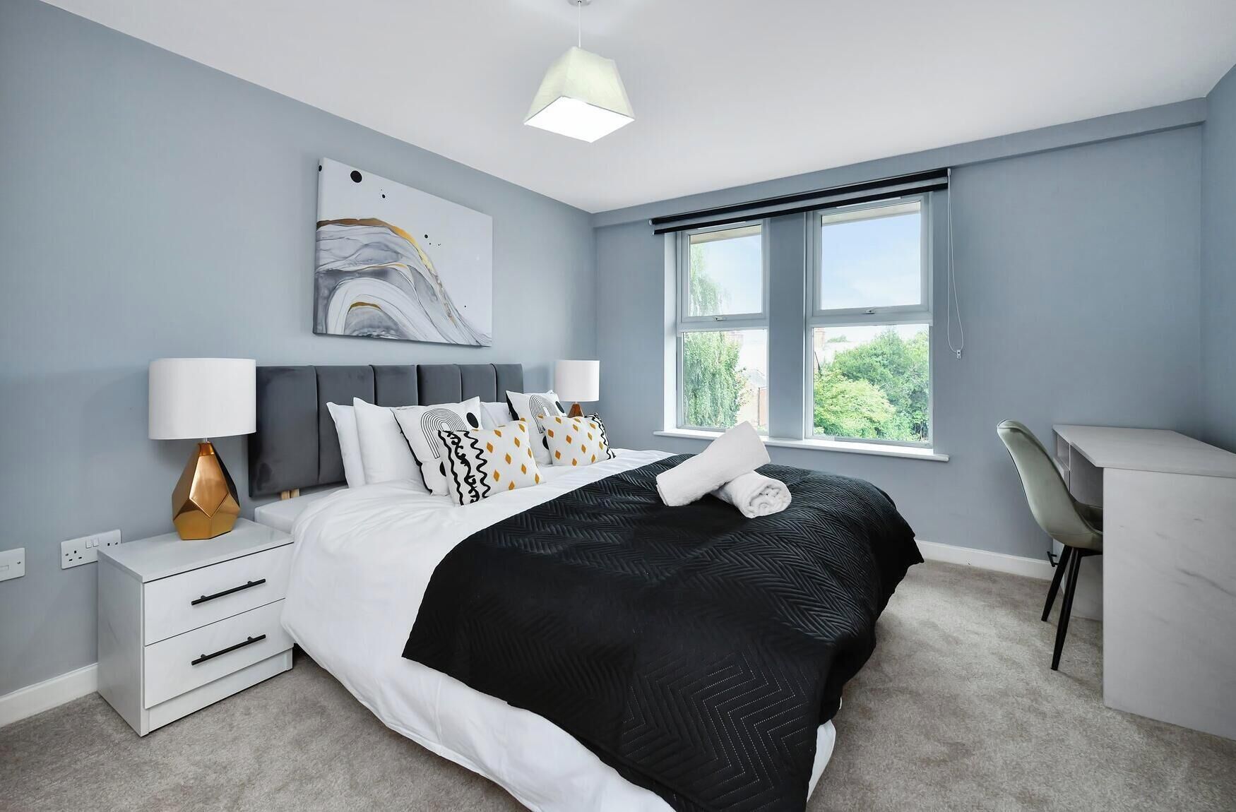 A modern bedroom with a bed, bedside table, lamp, and a desk with a chair.