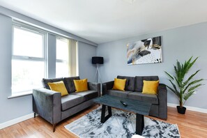 A living room with two grey sofas, yellow cushions, a black floor lamp, a painting, a potted plant, and a coffee table. - Modern 2-Bed Near Trent Bridge & City Ground (Nottingham)