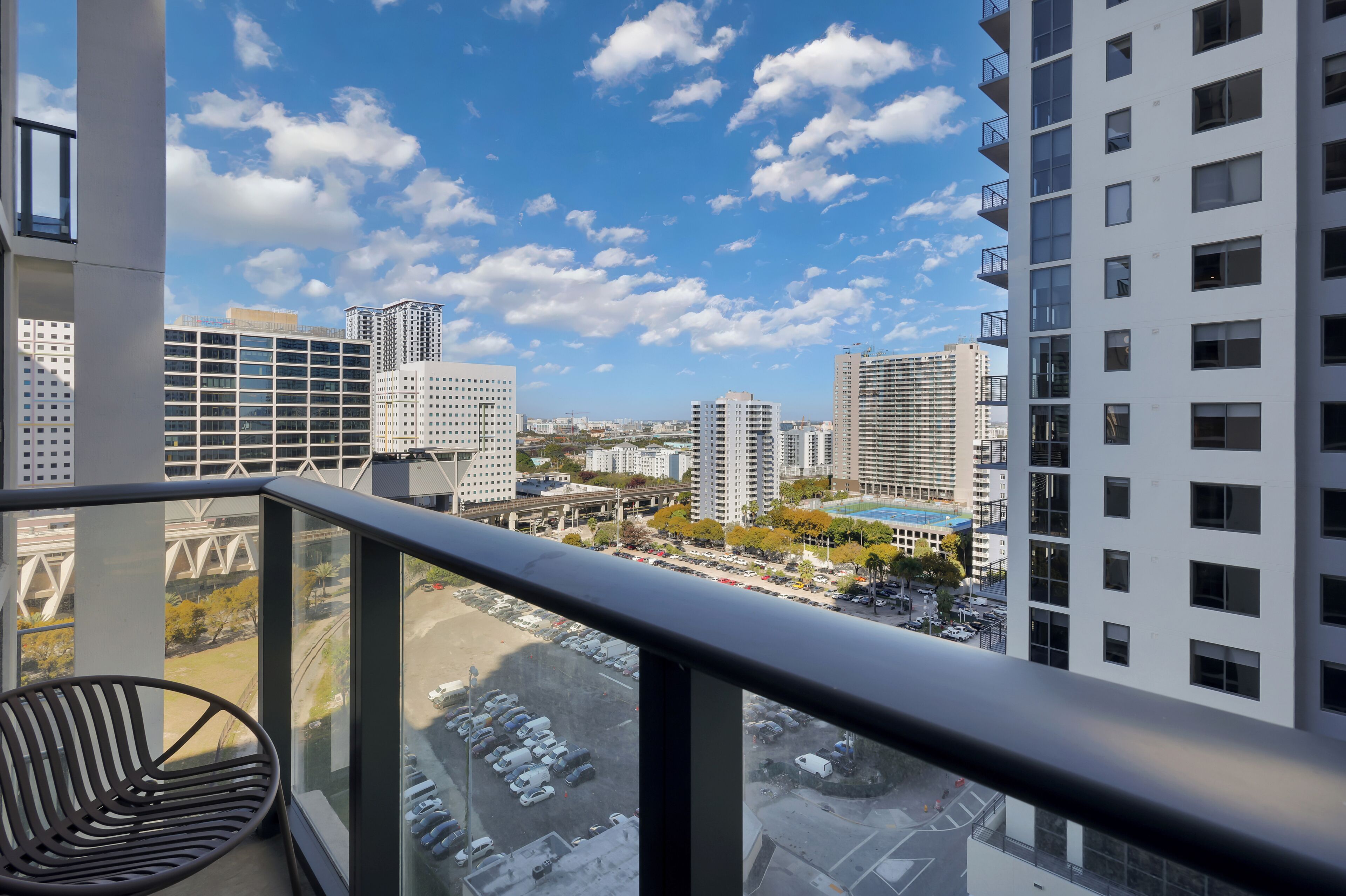 A balcony with a view of a cityscape, including high-rise buildings and a parking lot.