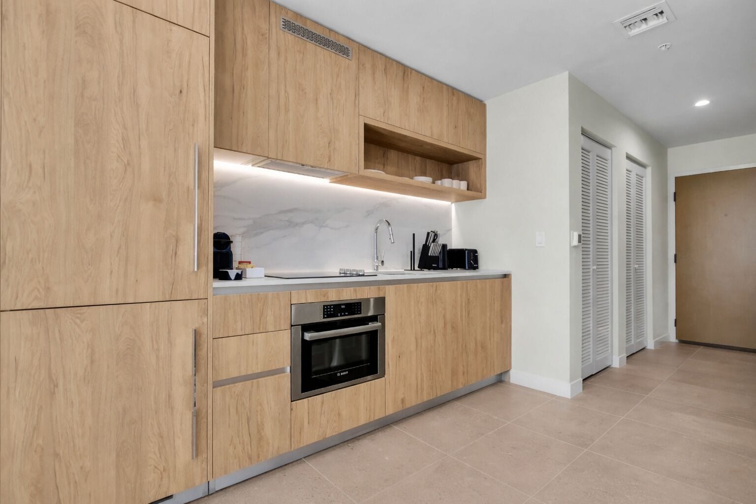 Una cocina moderna con armarios de madera, horno empotrado y encimera con pileta y grifo.