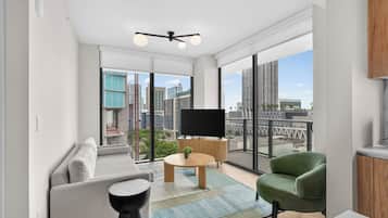 Una sala moderna con un sofá, un sillón verde, una mesita de centro y un televisor sobre un mueble.