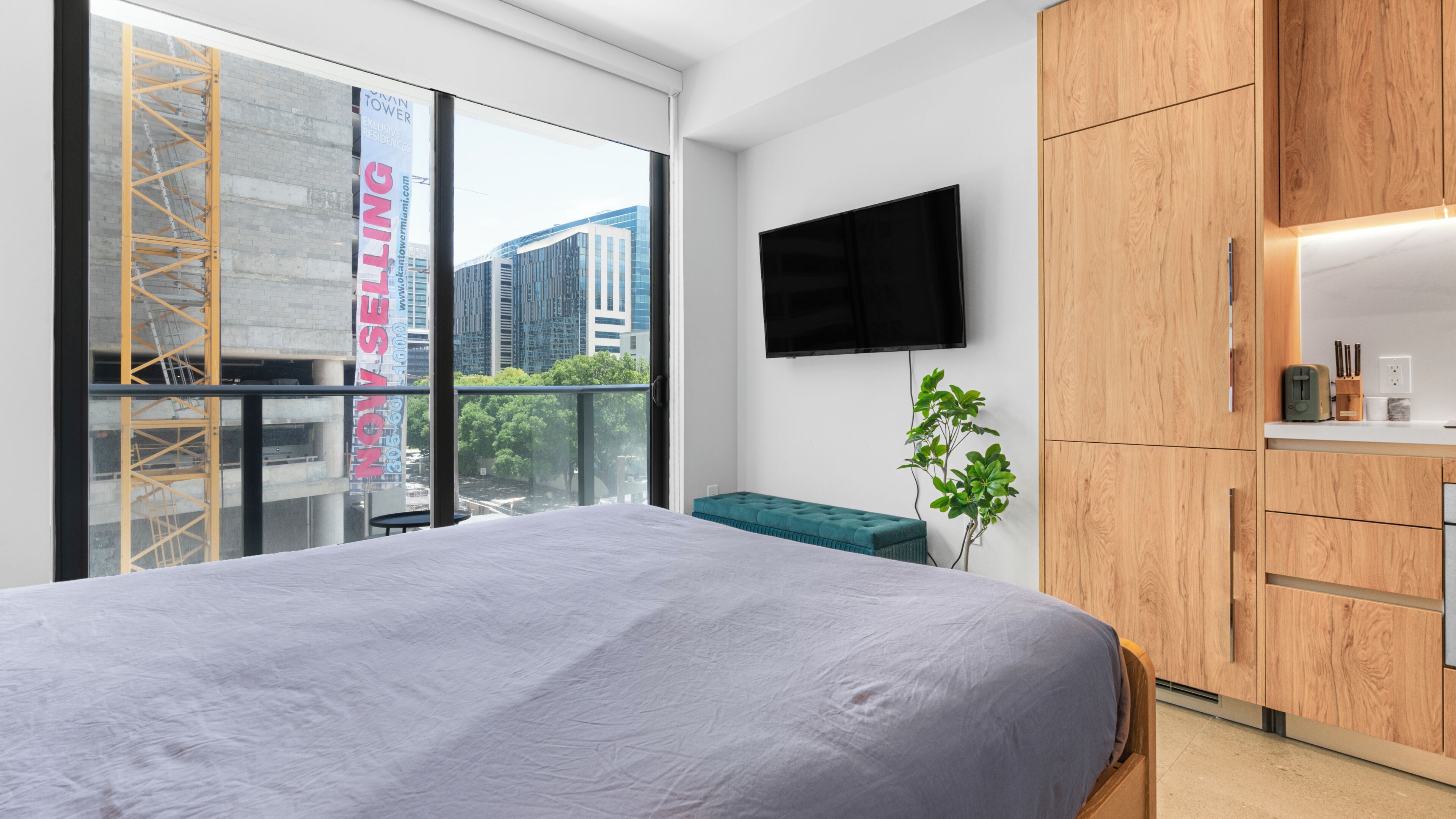 Habitación de hotel moderna con una cama grande, un televisor montado en la pared, un mueble de madera y vistas a la ciudad a través de un ventanal amplio.