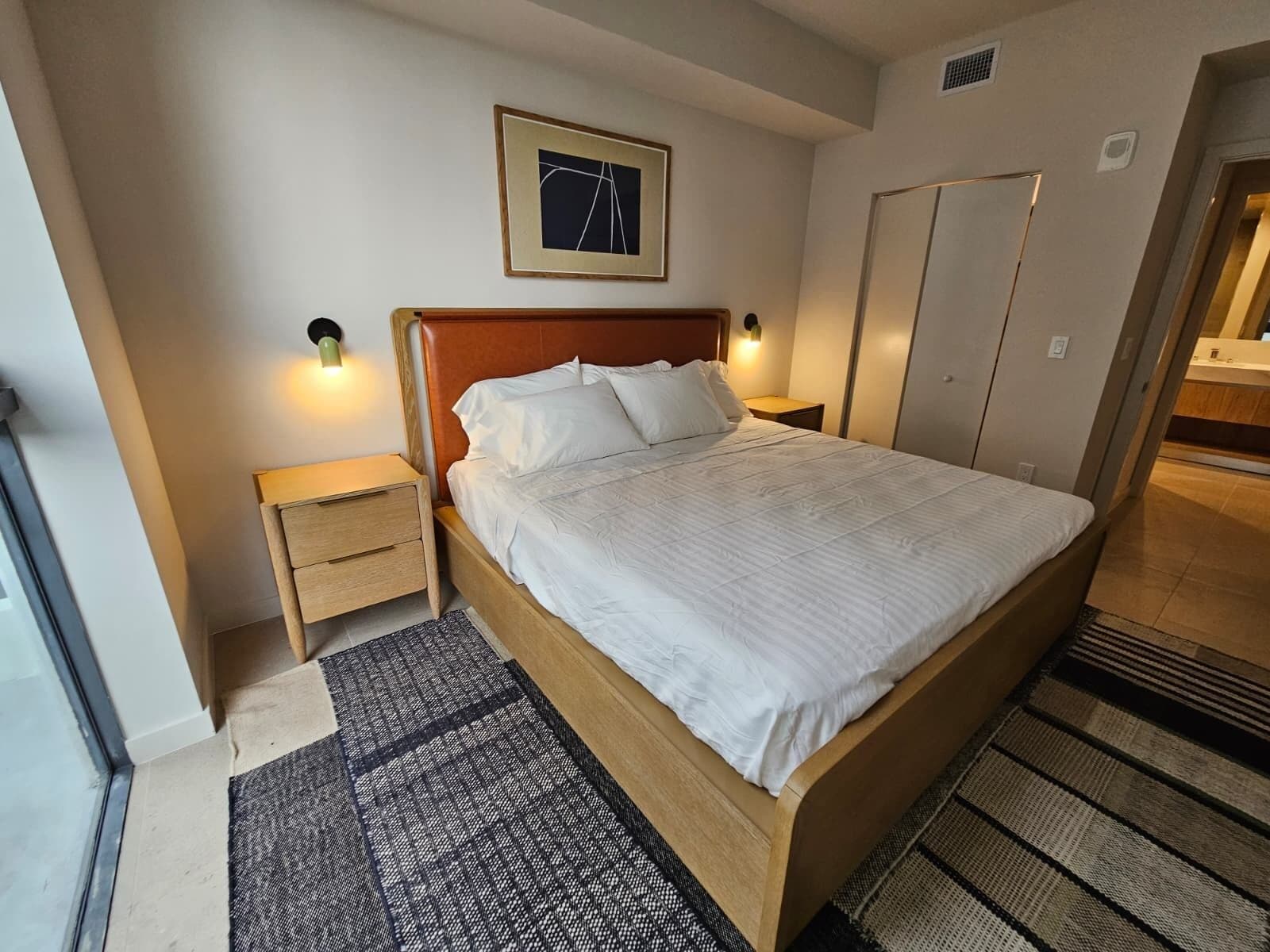 Une chambre d’hôtel avec un lit, des tables de chevet, un tableau accroché au mur et une porte de salle de bain.