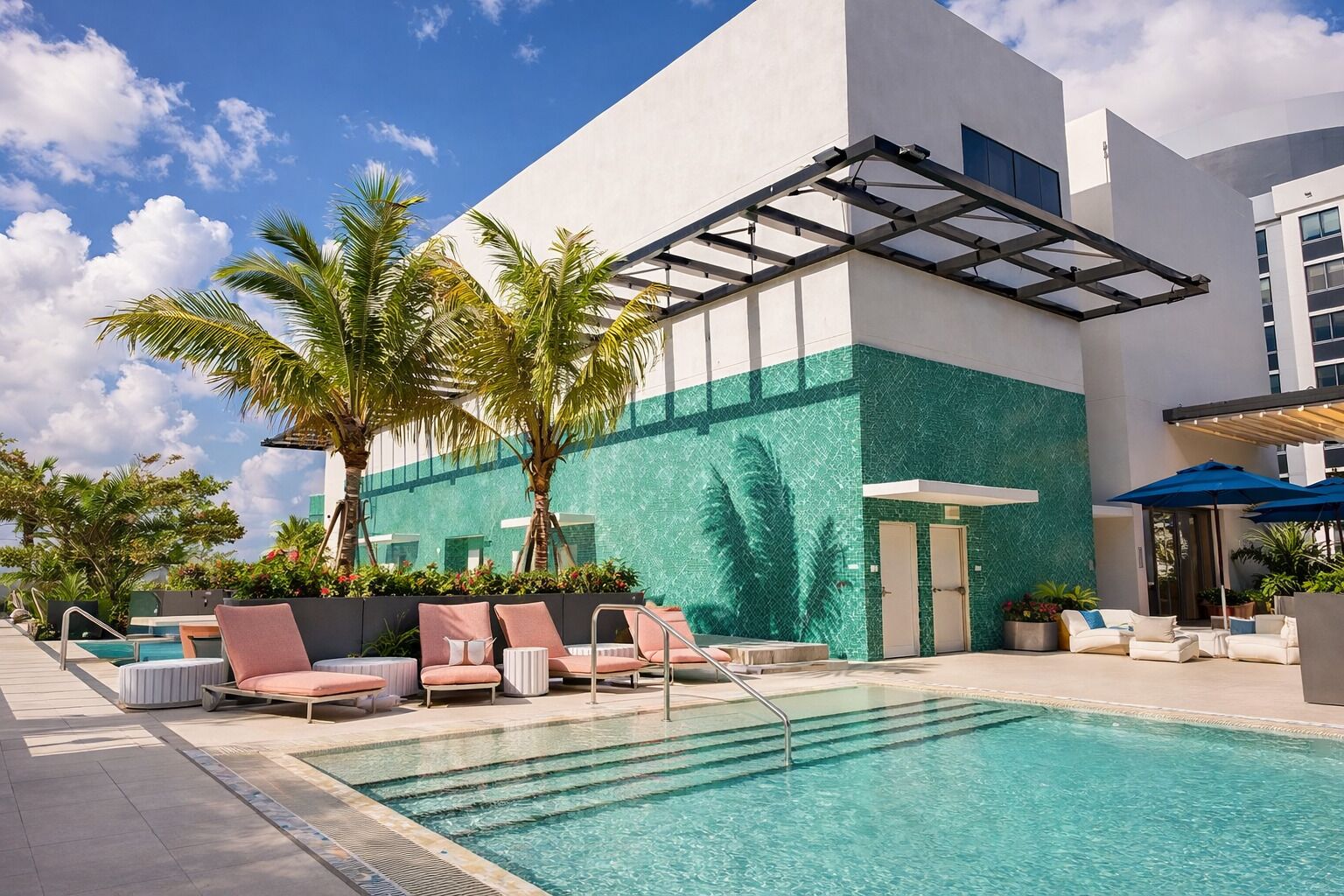 A modern hotel with a swimming pool, outdoor seating, and palm trees.