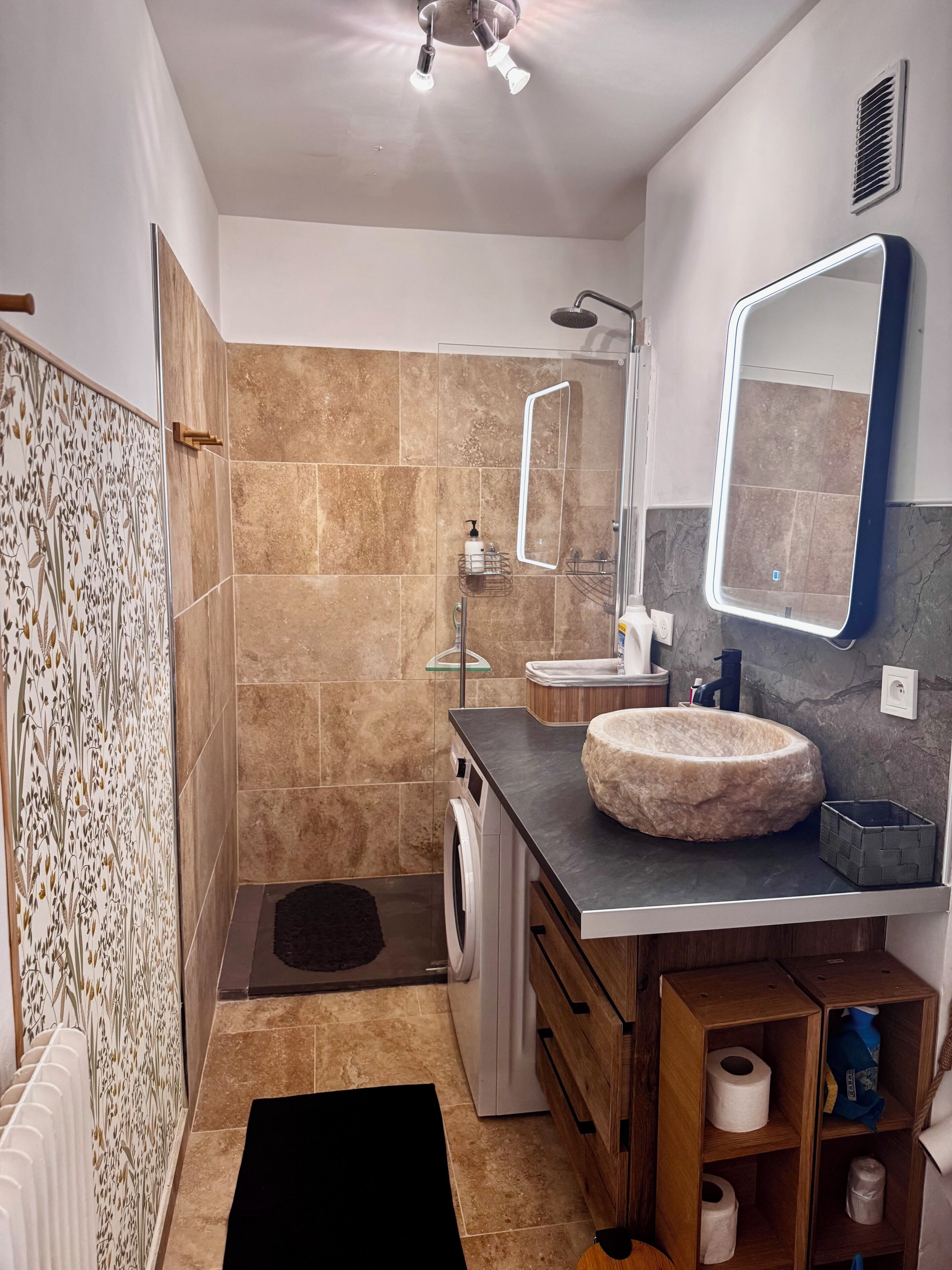 Un baño moderno con un espejo grande, un lavabo redondo y una ducha.