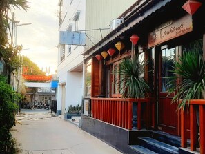 Vista de la calle con un edificio de fachada tradicional, una tienda con letrero y cielo despejado.