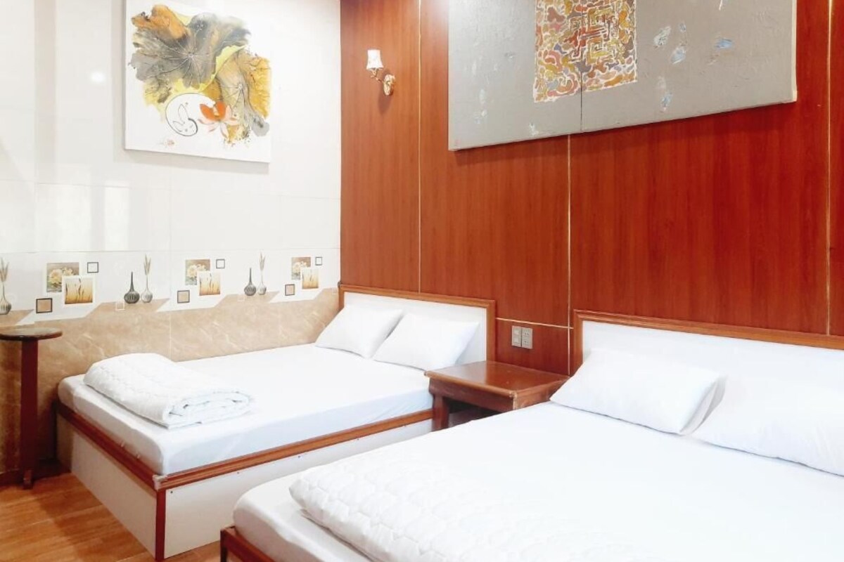 A hotel room with two single beds, a wooden headboard, a wall-mounted artwork, and a small bedside table with a lamp.