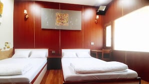 A hotel room with two beds, wooden flooring, a large window, and a wall-mounted artwork.