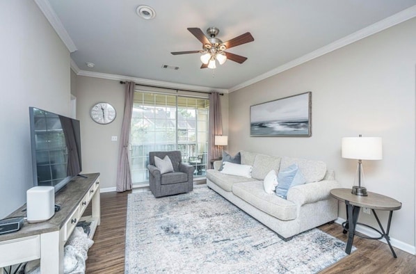 A living room with a sofa, armchair, TV, and a ceiling fan.