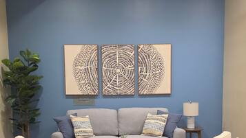 A living room with a grey sofa, two armchairs, a coffee table, and three wall art pieces.