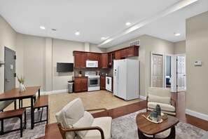 A modern kitchen with wooden cabinets, a microwave, oven, and refrigerator. There is a dining area with a table and chairs, and a living room with a sofa and coffee table. - Modern 2-bedroom by convention center -Elevator building (Philadelphia)