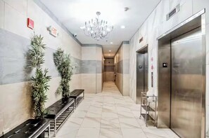 A hotel lobby with a marble floor, two potted plants, a bench, a chandelier, and two elevators. - Modern 2-bedroom by convention center -Elevator building (Philadelphia)