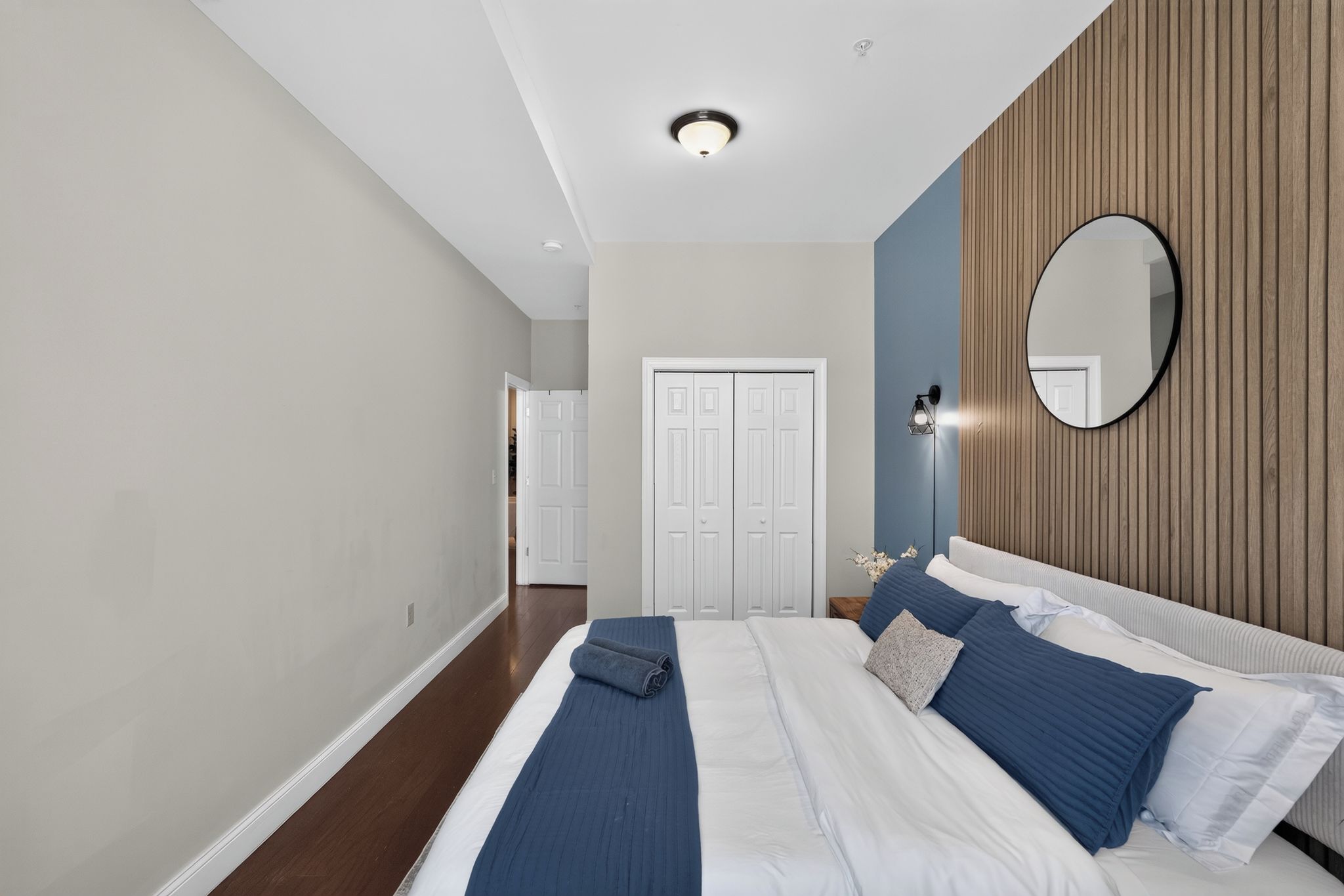 A bedroom with a large bed, a bedside table, a mirror, and a wardrobe.