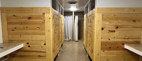 Un pasillo con literas de madera a ambos lados, que conduce a un baño con cortina de ducha.
