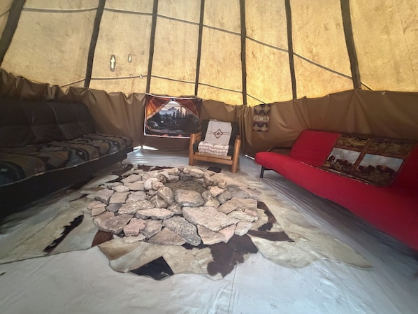 Interior de una tienda de campaña con un hogar de piedra, un sofá y una silla.