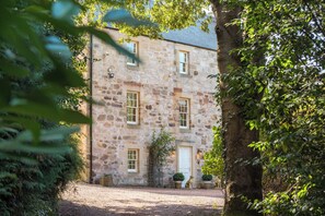 A stone building with a gravel driveway, a white door, and potted plants. - Luxury Scottish Country House Near Edinburgh (Dalkeith)