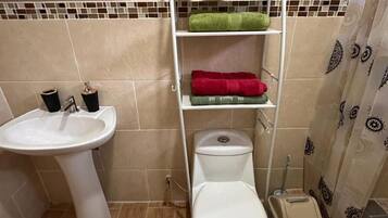 A bathroom with a white sink, toilet, and a shelf with towels and a vase.