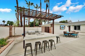 Eine Außenküche mit Grill, Barhocker und einer Pergola.