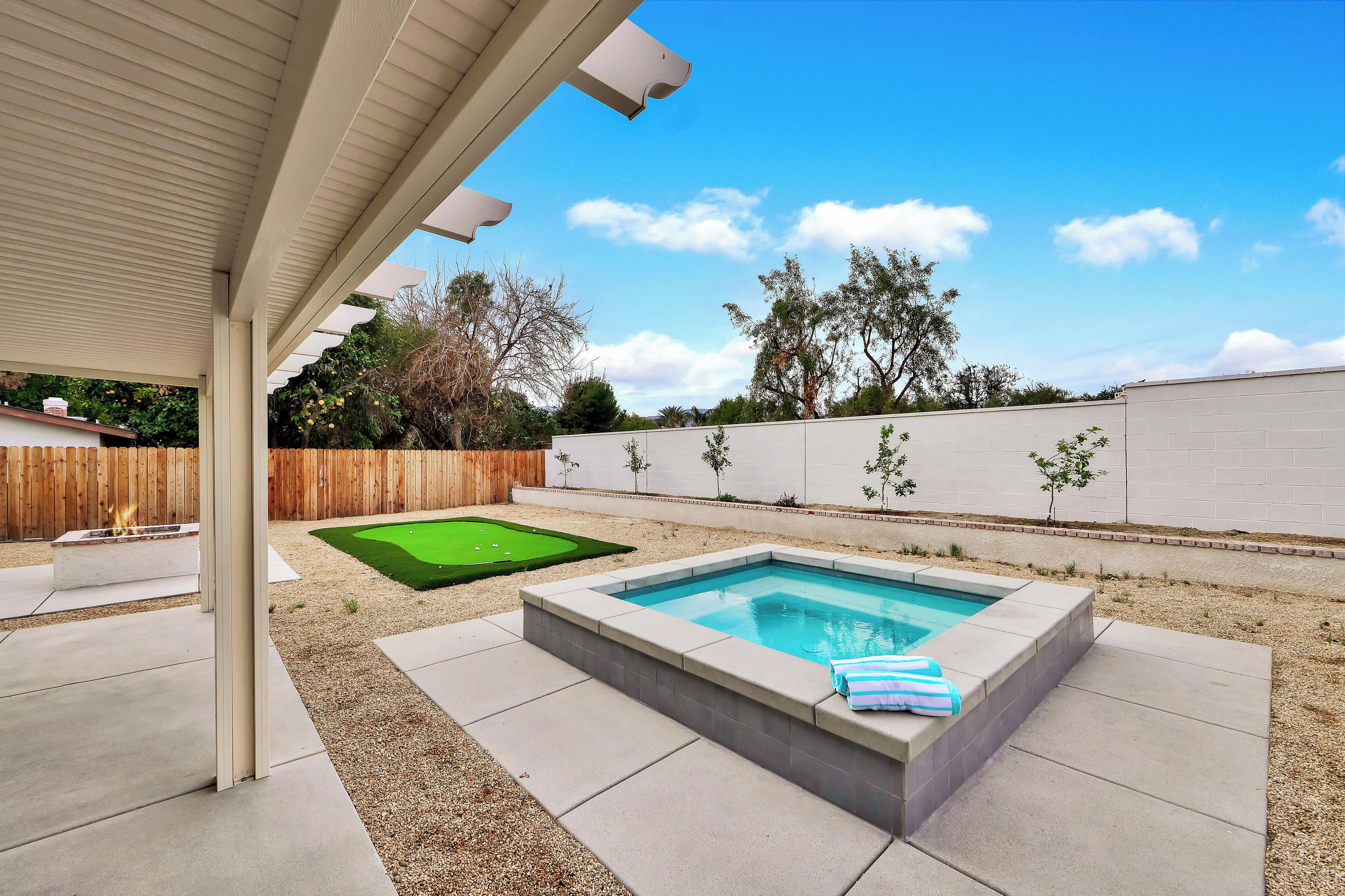 A backyard with a swimming pool, a fire pit, and a putting green.