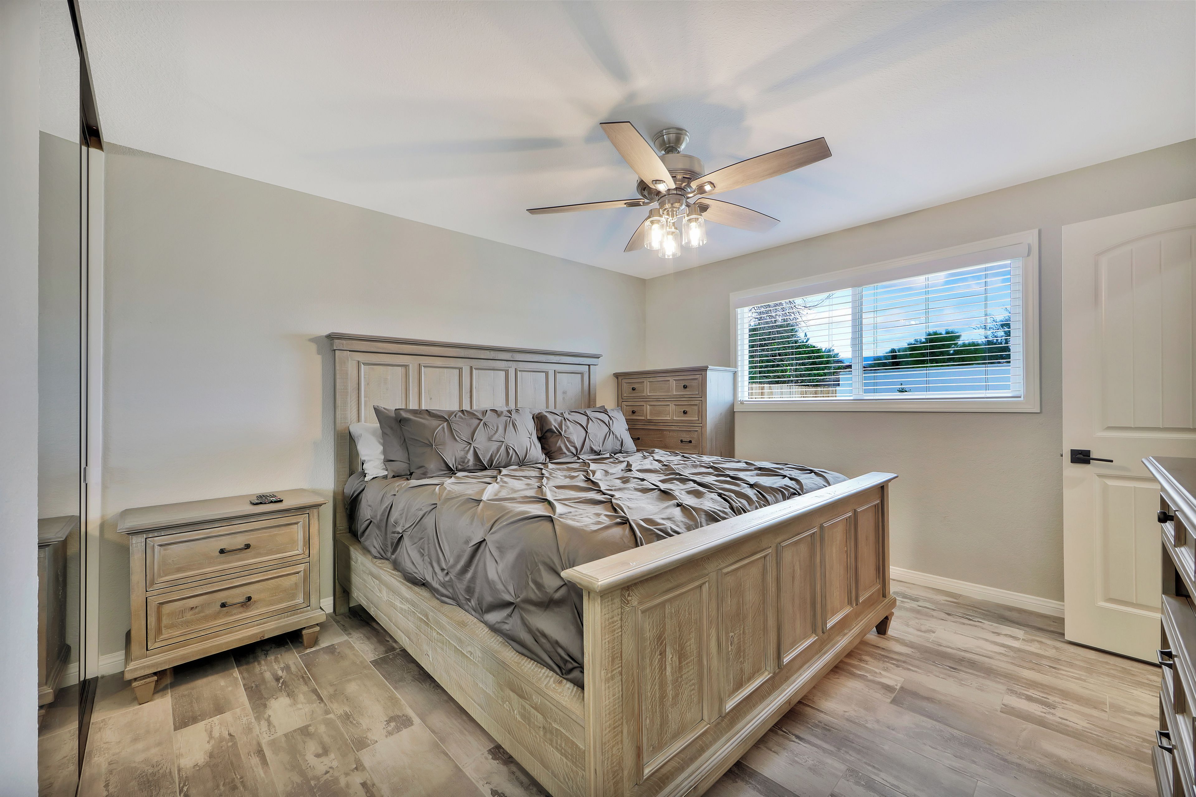 A bedroom with a wooden bed, a ceiling fan, a window with blinds, and a nightstand.