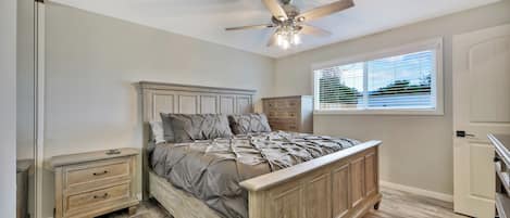 A bedroom with a wooden bed, a ceiling fan, a window with blinds, and a nightstand.