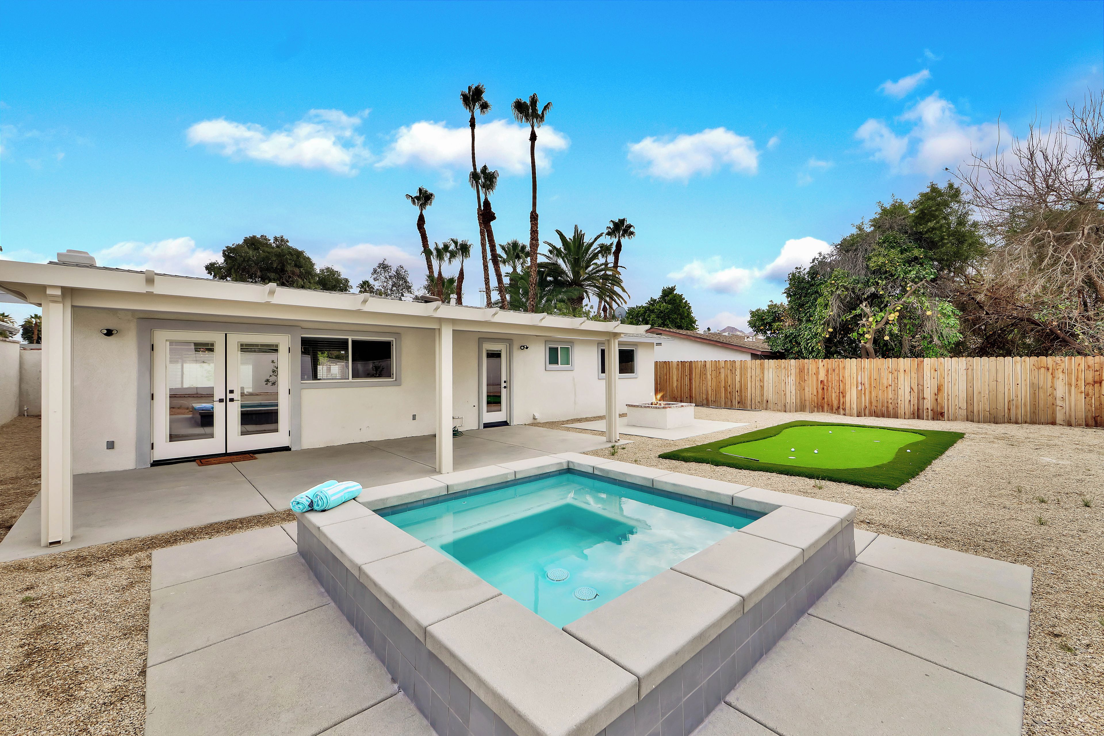 Una casa moderna con piscina, patio y jardín con césped y palmeras.