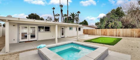 A modern house with a swimming pool, a patio, and a backyard with a lawn and palm trees.