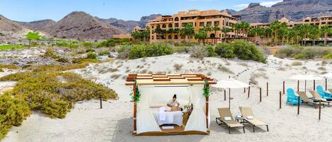 A desert resort with a massage tent, lounge chairs, and a building with palm trees in the background.
