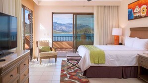 Habitación de hotel con cama, televisión, escritorio, silla, ventana con vista a las montañas y un cuadro en la pared.