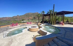 An outdoor pool area with lounge chairs, a fire pit, and a view of a mountainous landscape.